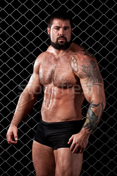 Stock photo: Bodybuilder posing in front of chain link.