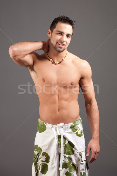 Attractive young man in boardshorts. Studio shot over grey. Stock photo © nickp37