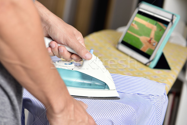 young man ironing a shirt while watching sports online Stock photo © nito