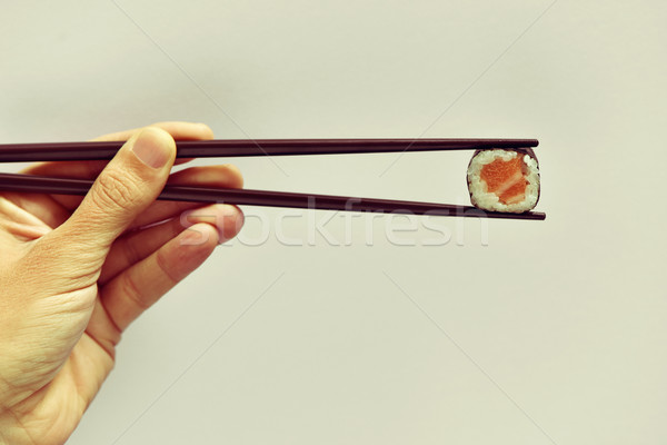 Stock photo: young man picking a makizushi with a pair of chopsticks