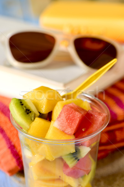 Foto stock: Ensalada · de · fruta · gafas · de · sol · libro · toalla · de · playa · primer · plano · plástico