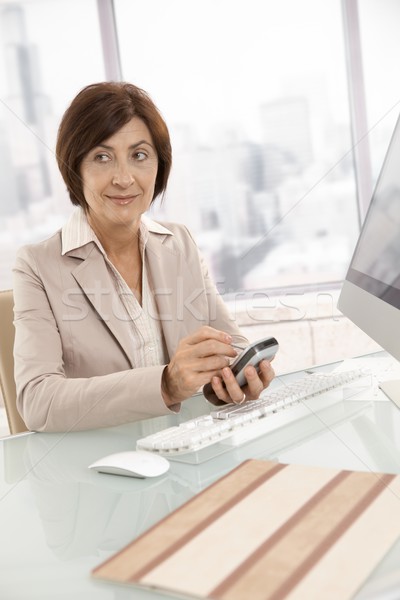 Stockfoto: Volwassen · zakenvrouw · smartphone · vergadering · bureau · glimlachend