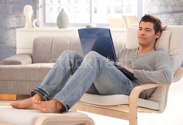 Stock photo: Goodlooking young man relaxing at home with laptop