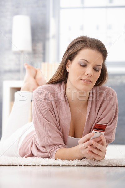 Smiling young woman using cellphone on floor Stock photo © nyul