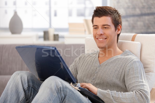 Stock photo: Smiling young man using computer in armchair