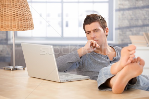Młody człowiek myślenia patrząc laptop posiedzenia domu Zdjęcia stock © nyul
