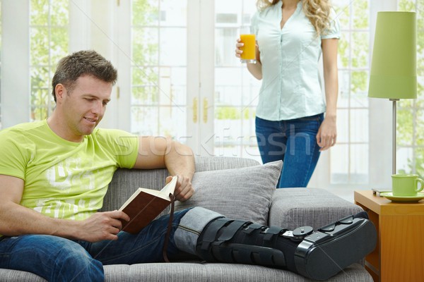 Om picior rupt lectură carte canapea acasă Imagine de stoc © nyul