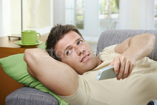  Smiling man on sofa using remote control Stock photo © nyul