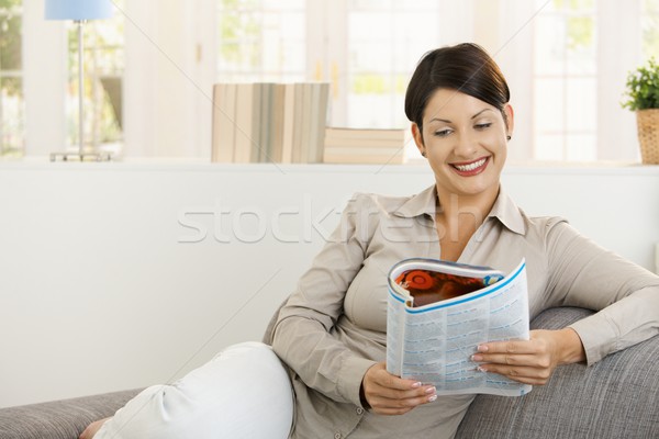 Stock photo: Happy woman reading newspaper on sofa