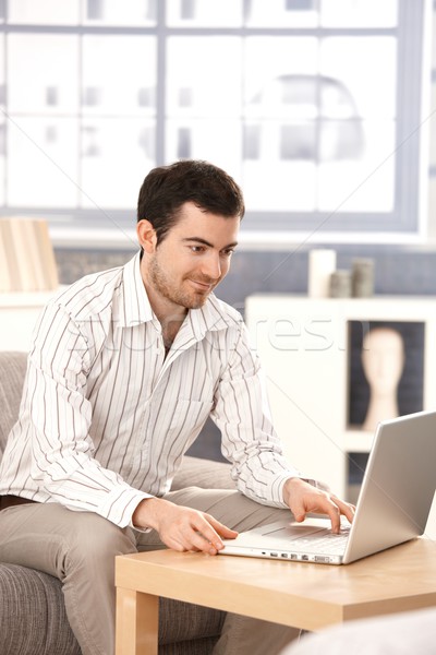 Stock photo: Young man browsing internet at home smiling