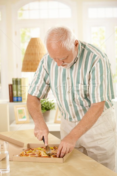 Elderly man slicing up pizza. Stock photo © nyul