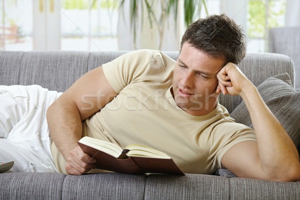 Stock photo:  Smiling man lying on sofa reading