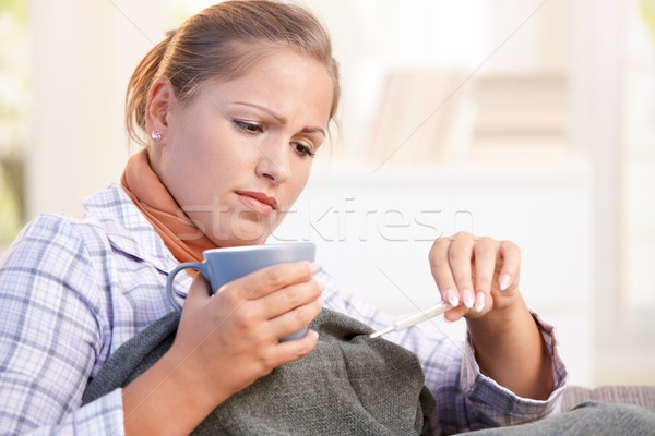Stock photo: Young woman having flu taking her temperature