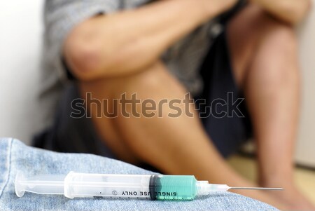 Syringe and sick male addict crouched in background Stock photo © palangsi