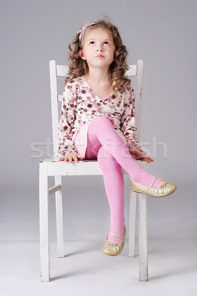 Sweet little girl sitting on the white chair looking away maki