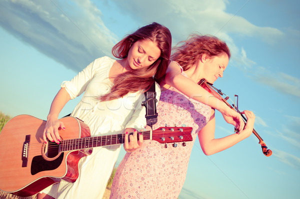 Two young women playing guitar and violin outdoors. Split toning Stock photo © pekour