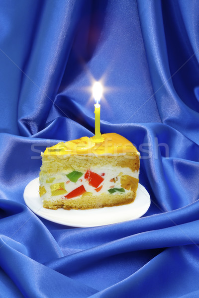 piece of fruit jelly cake with a lighted candle on a background of blue silk Stock photo © Photocrea