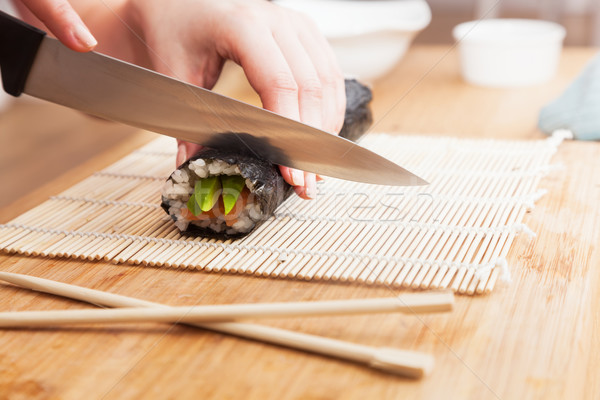 Stock photo: Preparing sushi, cutting. Salmon, avocado, rice and chopsticks on wooden table. 