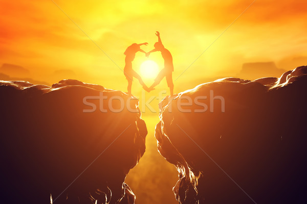 Happy couple in love making heart shape over precipice at sunset. Stock photo © photocreo