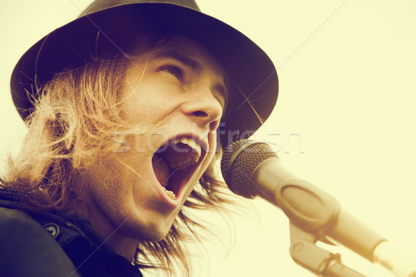 Young man with long hair and hat shouting to microphone. Vintage, music Stock photo © photocreo