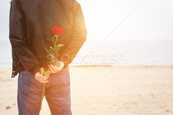 Stock photo: Man with a rose behind his back waiting for love. Romantic date on the beach