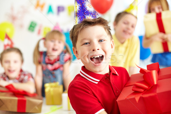 Joyful boy with giftbox looking at camera with his friends on background Stock photo © pressmaster