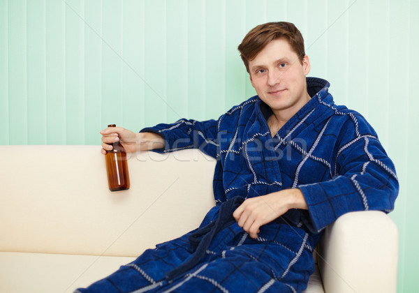 Young man drinks beer in dressing gown on sofa Stock photo © pzaxe