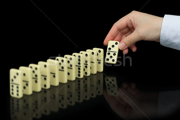 Hand builds a line of dominoes on black background Stock photo © pzaxe