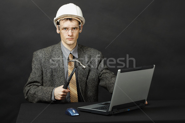 Stock photo: Man in helmet with hammer repairs computer