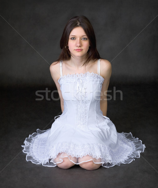 Stock photo: Girl in a white dress sits on a black background