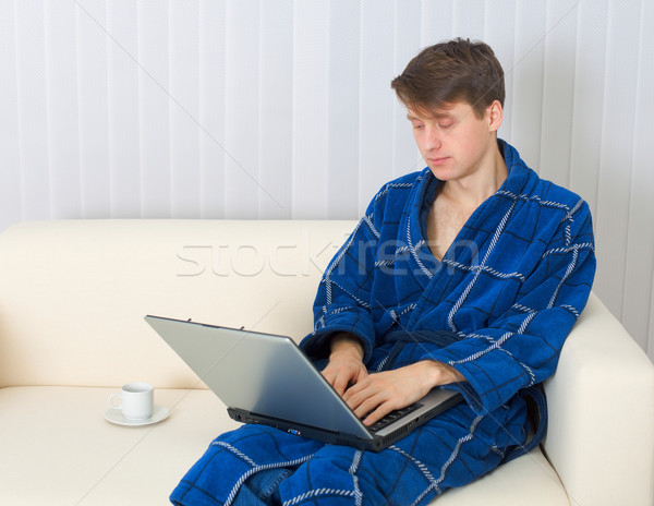 Young man works with laptop in blue dressing gown Stock photo © pzaxe