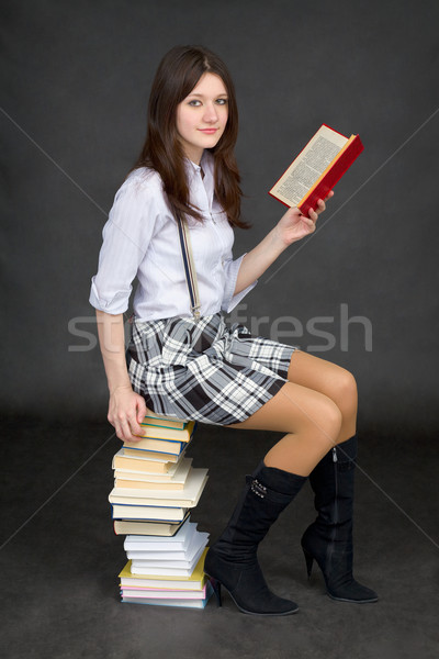 Stock photo: Beautiful young woman reads on a pile of books on black backgrou