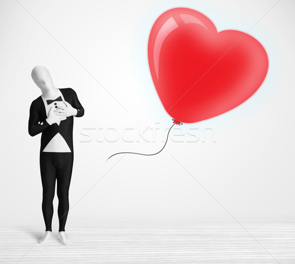 Cute guy in morpsuit body suit looking at a red balloon shaped heart Stock photo © ra2studio