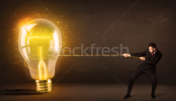Business man pulling a big bright glowing light bulb Stock photo © ra2studio