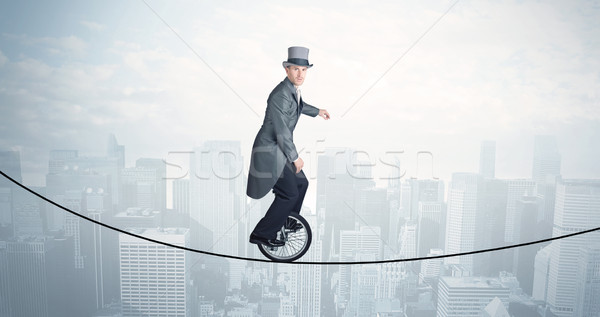 Brave guy riding a monocycle on a rope above cityscape Stock photo © ra2studio