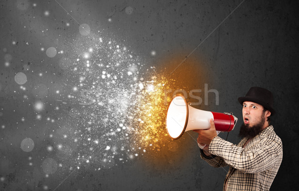 Guy shouting into megaphone and glowing energy particles explode Stock photo © ra2studio