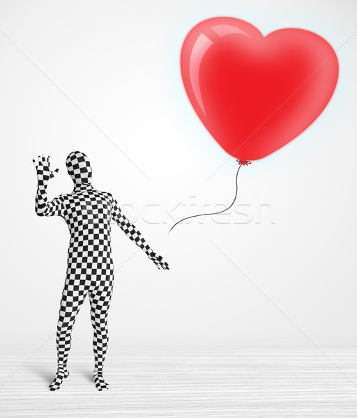 Cute guy in morpsuit body suit looking at a red balloon shaped heart Stock photo © ra2studio