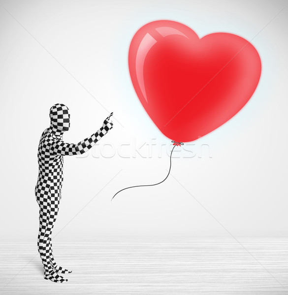 Cute guy in morpsuit body suit looking at a red balloon shaped heart Stock photo © ra2studio