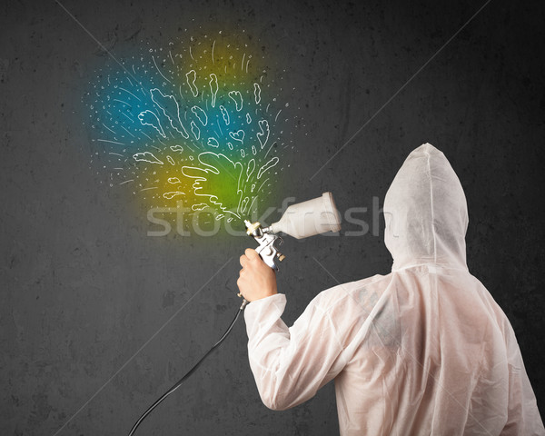 Stock photo: Worker with airbrush gun paints colorful lines and splashes