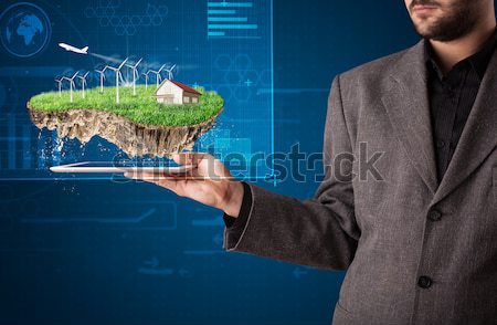 Stock photo: Young businessman presenting a perfect ecology land with a house and windmills