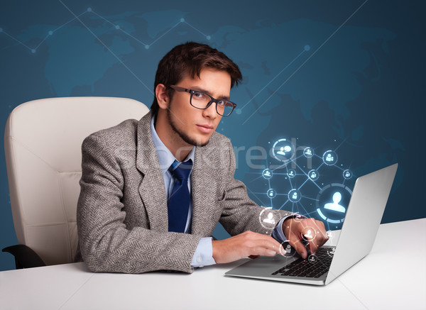 Attractive young man sitting at desk and typing on laptop with social network icons comming out Stock photo © ra2studio