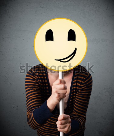 Stock photo: Young woman holding a smiley face emoticon