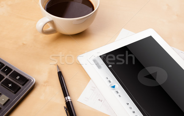 Stock photo: Workplace with tablet pc showing media player and a cup of coffee on a wooden work table closeup