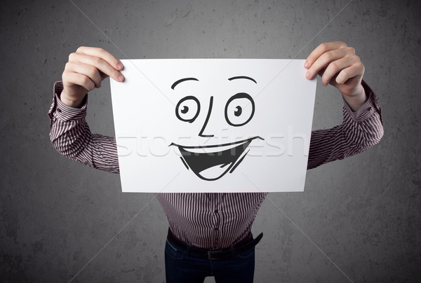 Stock photo: Businessman holding a cardboard with smiley face on it in front 