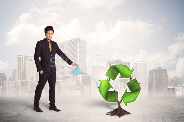 Stock photo: Business man watering green recycle sign tree on city background