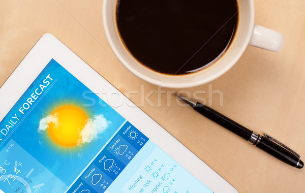 Workplace with tablet pc showing weather forecast and a cup of coffee on a wooden work table closeup Stock photo © ra2studio