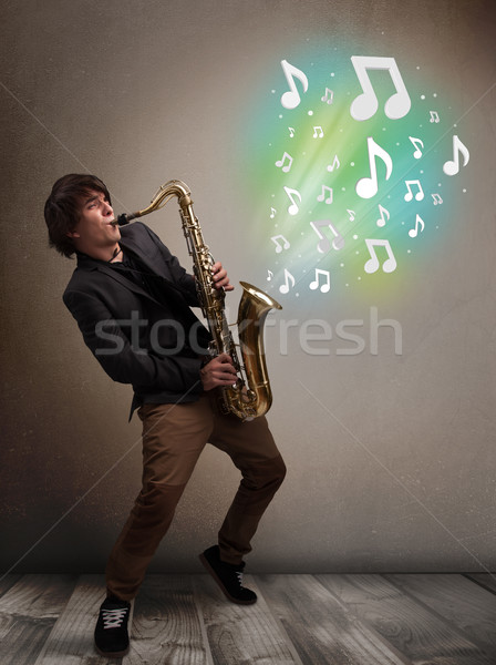 Young musician playing on saxophone while musical notes explodin Stock photo © ra2studio