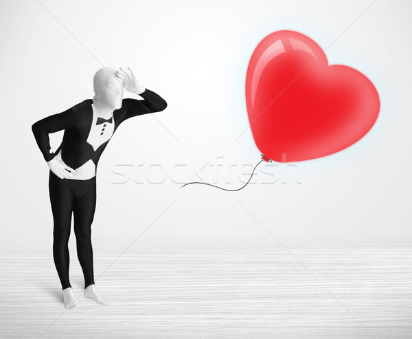 Cute guy in morpsuit body suit looking at a red balloon shaped heart Stock photo © ra2studio