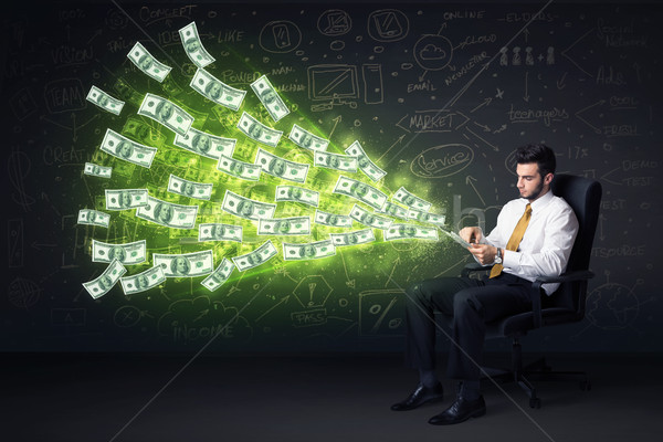 Stock photo: Businessman sitting in chair holding tablet with dollar bills co