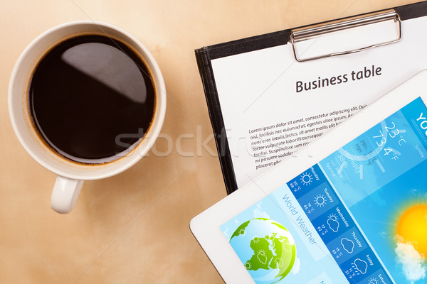 Stock photo: Workplace with tablet pc showing weather forecast and a cup of coffee on a wooden work table closeup